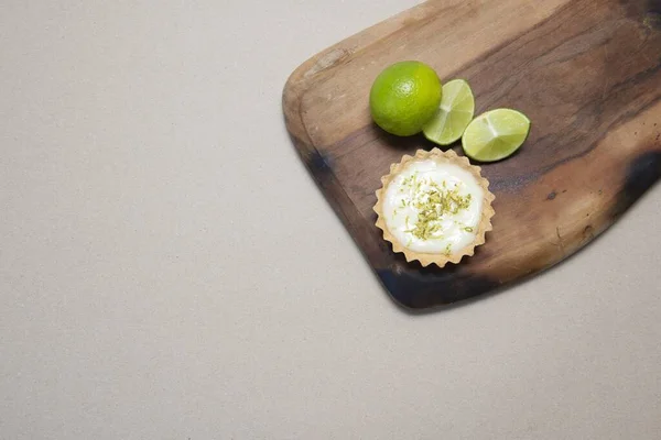 A top view of a key lime tartlet on a wooden board with key lime fruits and a space for your text