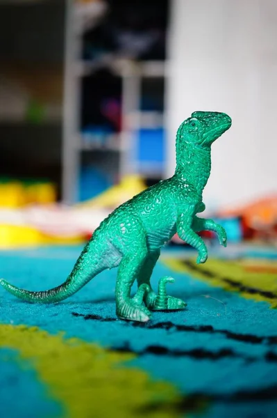 A closeup of a green toy dinosaur on a blue carpet under the lights with a blurry background