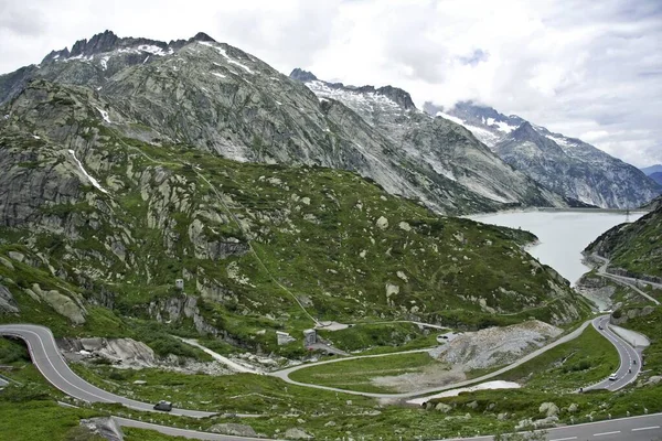 Uma Vista Uma Estrada Lago Cercado Por Montanhas Altas Cobertas — Fotografia de Stock