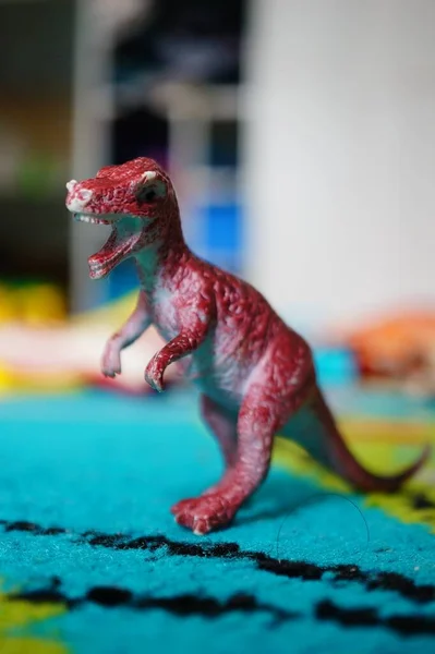 在灯光下的蓝色地毯上 一个红色咆哮的玩具恐龙的垂直镜头 背景模糊不清 — 图库照片