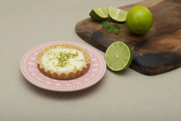A soft focus of a key lime tartlet on a plate with key lime fruits on a wooden board