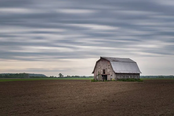暗い曇り空の下で一人で畑に立っている木製の納屋の劇的なショット — ストック写真