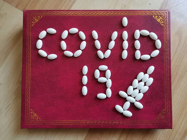 Napis Covid19 Wykonany Białych Tabletek Burgundowej Tablicy Złotymi Wzorami — Zdjęcie stockowe