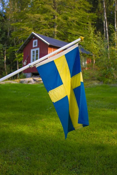 瑞典国旗蓝色 黄色的十字在风中飘扬 后面是一座木制房屋 — 图库照片