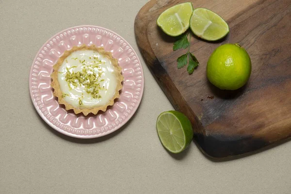 A top view of a key lime tartlet on a wooden board with some slices key lime fruits