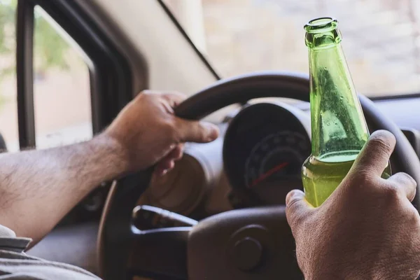 A man driving a car while holding a bottle of beer. Drunk diving, unsafe driving concept