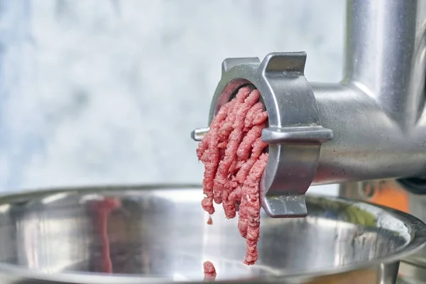 A closeup of ground meat coming out of an electric meat grinder