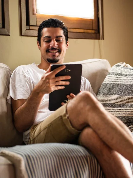 Una Foto Hombre Moreno Sentado Sofá Blanco Sosteniendo Una Tableta — Foto de Stock