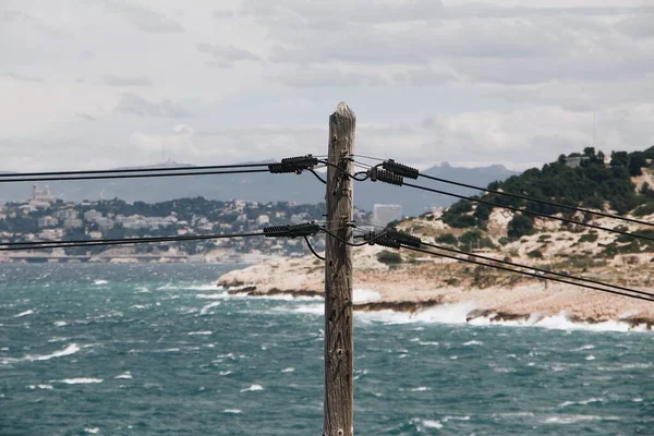 A peaceful scene of overhead power lines on a background of a quiet sea and huge rocks, Marseille, Spain