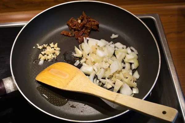 木製のスプーンでフライパンに油 玉ねぎ ニンニク 乾燥トマトのクローズアップショット — ストック写真
