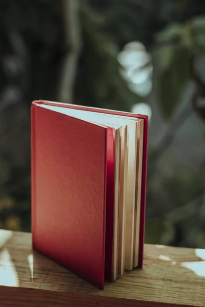 Pionowe Ujęcie Książki Czerwoną Okładką Drewnianym Płocie Ogrodzie Pod Słońcem — Zdjęcie stockowe