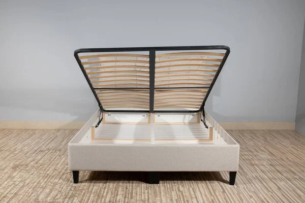 A beige bed with a storage space revealed by lifting the wooden slatted base