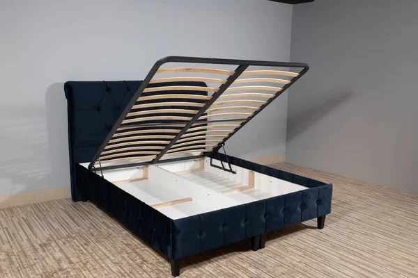 A dark blue bed with a storage space revealed by lifting the wooden slatted base