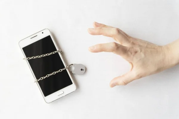 A reaching hand next to a white phone tied in a chain and a lock showing the concept of phone addiction