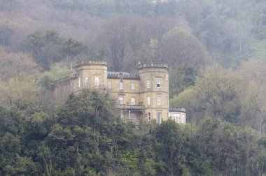 A horizontal view of a huge stone house surrounded by trees in a light fog, San Sebastian, Spain clipart