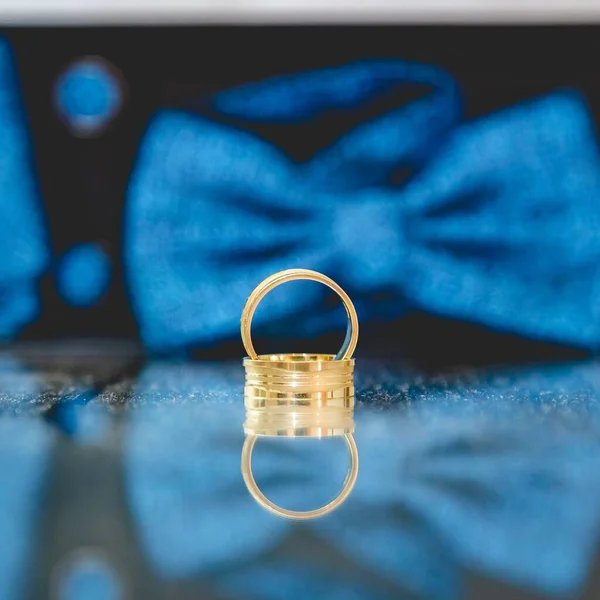 背景に青の蝶ネクタイを持つミラー上の黄金の結婚指輪の選択的なフォーカスショット — ストック写真