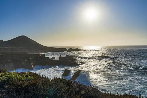 輝く太陽の下で高い岩の崖を打つ美しい波状の海 — ストック写真