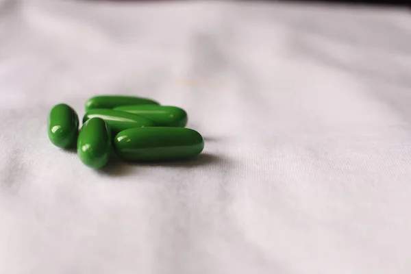 白い布の上に緑の丸薬の浅いフォーカスクローズアップショット — ストック写真
