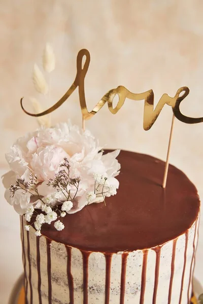 白い背景の白いテーブルの上にチョコレートドリップと愛のトッパーとおいしいウェディングケーキの垂直クローズアップショット — ストック写真