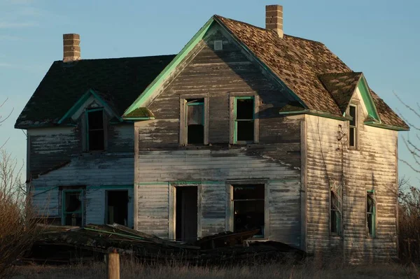 A creepy, old and aged abandoned wooden house in a field under the blue sky