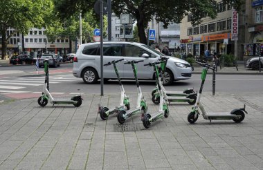 COLOGNE, GERMANY - Jun 20, 2020: Cologne, Germany - June 20, 2019: E-mobility in Germany: E-scooters waiting for customers next to a road in Cologne, Germany, as cars go by clipart