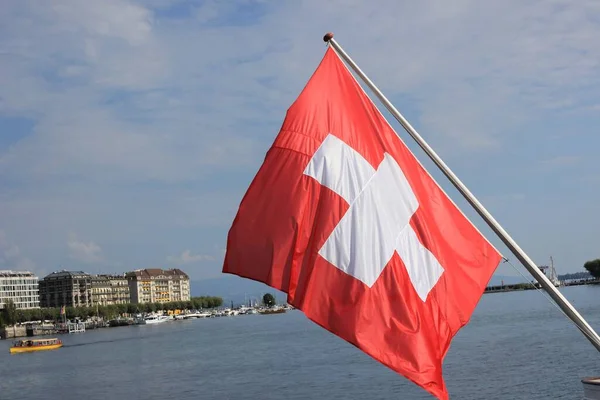 在以建筑物为背景的水边选择性地拍摄了一面瑞士国旗的焦点 — 图库照片