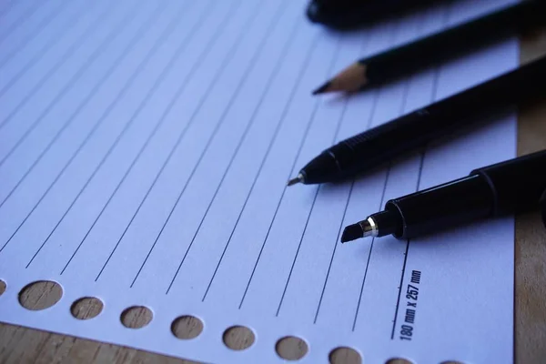 ペンと鉛筆のクローズアップショットが並んでいるノートブックのページに — ストック写真