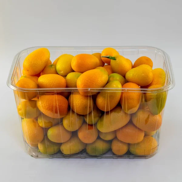 在灰色背景下隔离的塑料容器中的整个Kumquats的特写镜头 — 图库照片