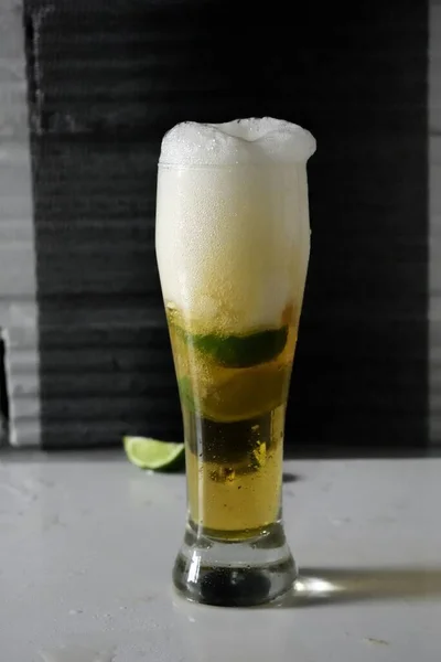 Colpo Verticale Bicchiere Birra Fredda Con Fette Lime Tavolo Bianco — Foto Stock