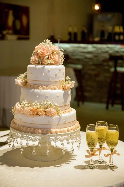 一张垂直的特写照片 是一个漂亮的三层蛋糕 桌上摆放着玫瑰装饰和香槟酒杯 — 图库照片