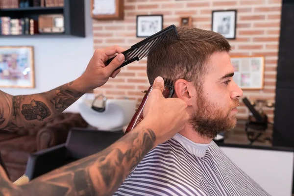 Młody Fryzjer Obcinający Męskie Włosy Maszynką Strzyżenia Grzebieniem Zakładzie Fryzjerskim — Zdjęcie stockowe