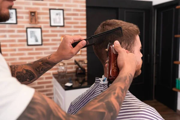 Młody Fryzjer Obcinający Męskie Włosy Maszynką Strzyżenia Grzebieniem Zakładzie Fryzjerskim — Zdjęcie stockowe