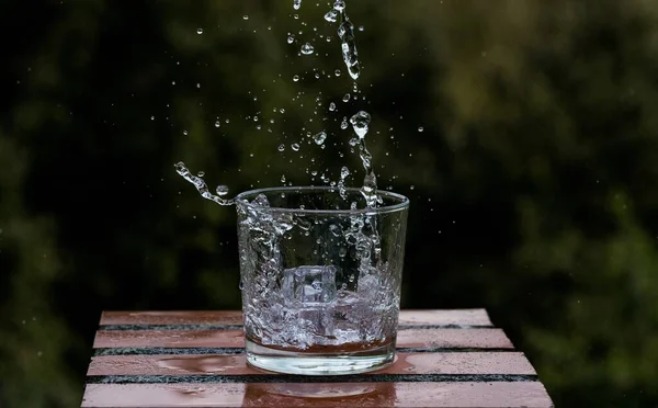 Ein Spritzer Eiswürfel Einem Glas Erfrischungsgetränk Auf Verschwommenem Hintergrund — Stockfoto
