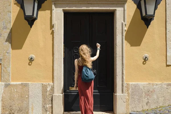 一个穿着红色衣服的年轻女子白天在阳光下敲着门 — 图库照片