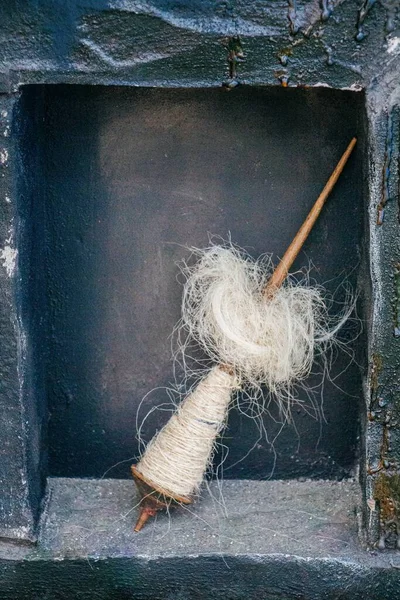 A vertical image of tangled white thread wrapped around a wooden spindle