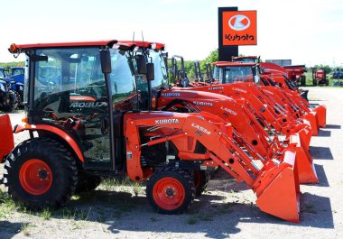 CHESLEY, CANADA - Jun 06, 2020: Row of Kubota loader tractors at dealership with sign behind on a sunny spring day clipart