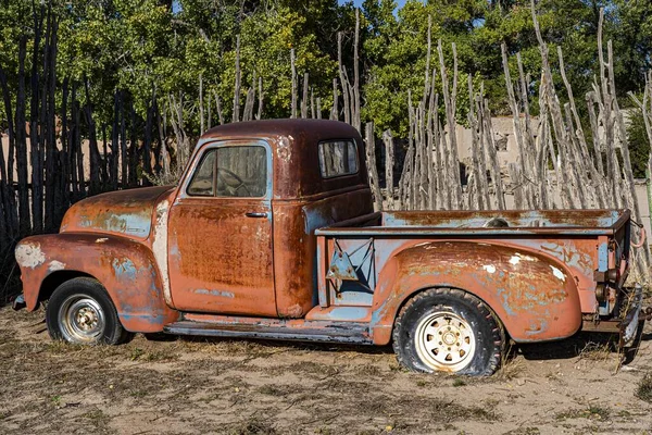 An old abandoned rusty truck in a dry field with a wooden fence