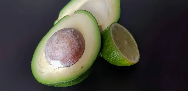 Avocado Limoen Helften Een Zwarte Achtergrond — Stockfoto