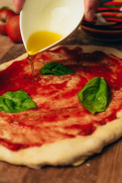 自家製ピザにオリーブオイルを注ぐ人のクローズアップショット マリナラソースとバジルの葉と — ストック写真