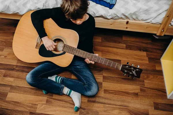 A young boy holding a guitar and sitting on the floor