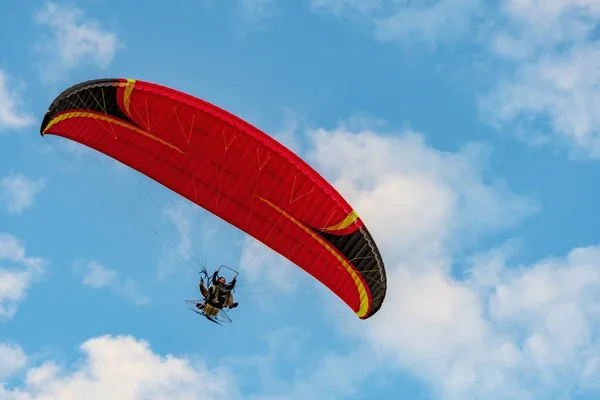 Red dome of a motor paraglider flying on a background of blue cloudy summer sky. Tandem on a paraglider high in the sky.