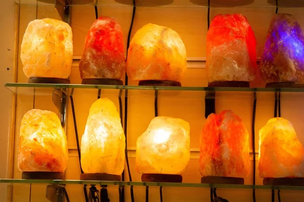 A closeup shot of lit salt lamps displayed on glass shelves with yellow wall as background