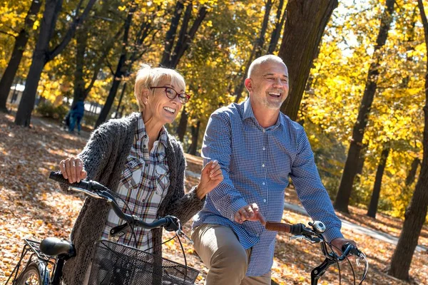 An old laughing couple riding bicycles in the park in autumn at daytime - happiness concept