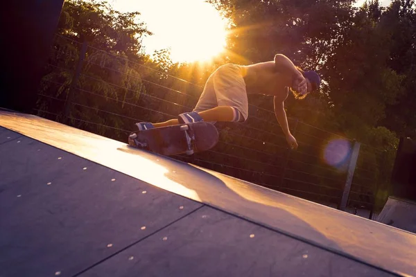 太陽の光の下で木々に囲まれた公園で若い男性のスケートボード — ストック写真