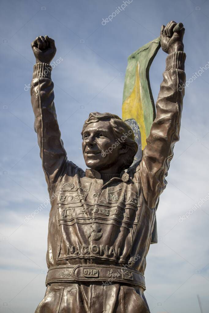 RIO DE JANEIRO, BRAZIL - Jul 12, 2020: Bronze statue of Ayrton Senna holding a Brazilian flag up high with his racing suite full of company sponsor logos on Copacabana boulevard