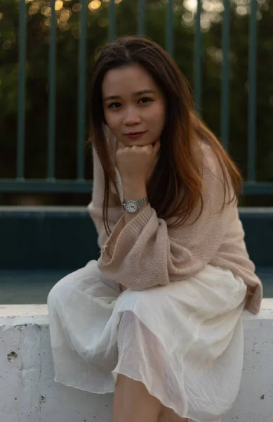 Beyaz Elbiseli Asyalı Bir Kadının Arka Planda Çitle Oturduğu Dikey — Stok fotoğraf