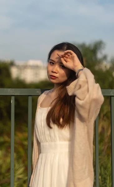 Beyaz Elbiseli Asyalı Bir Kadının Arka Planda Çitle Dikey Görüntüsü — Stok fotoğraf