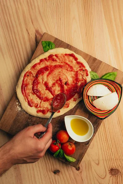 自家製ピザを作る人のオーバーヘッドショット マリナラソースと オリーブオイル 新鮮なモッツァレラ バジルの葉 — ストック写真