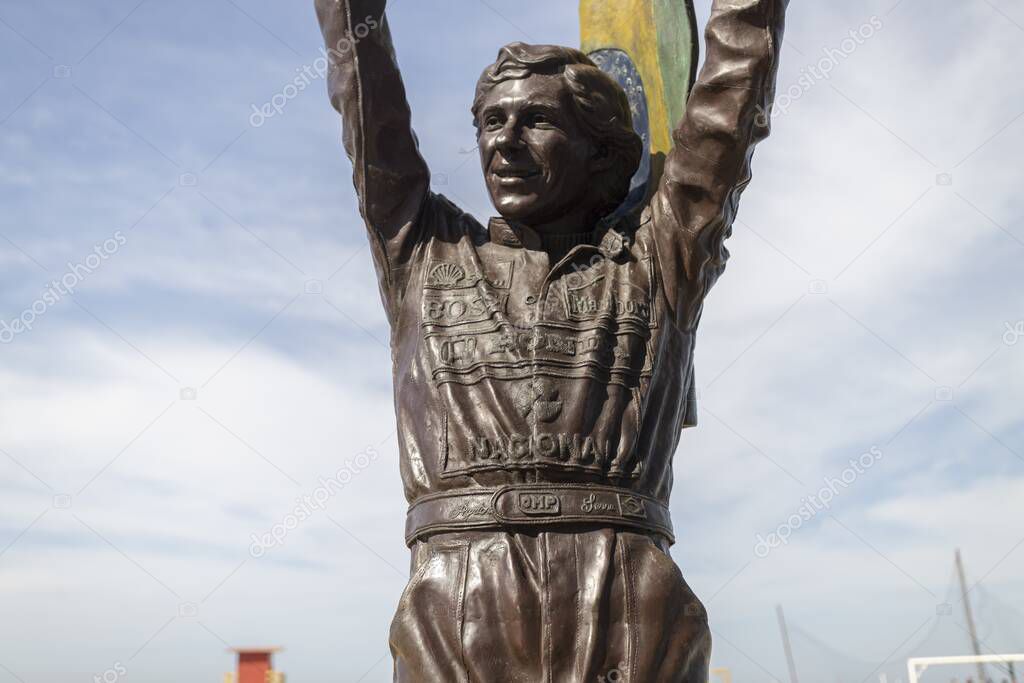 RIO DE JANEIRO, BRAZIL - Jul 12, 2020: Bronze statue of Ayrton Senna holding a Brazilian flag up high with his racing suite full of company sponsor logos on Copacabana boulevard