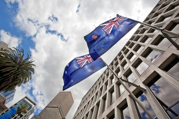 A low angle shot of Australian flags waving from a Government Building against a cloudy sky